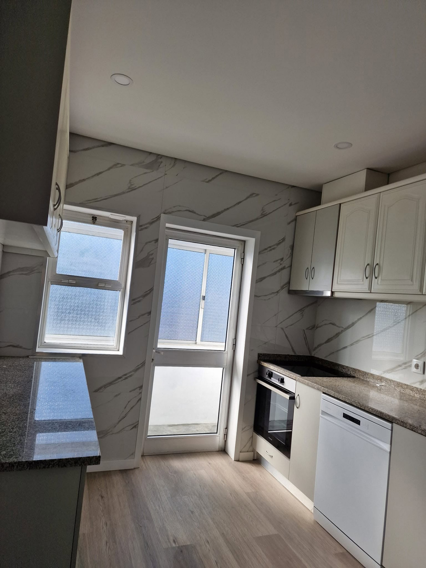 Cozinha do apartamento T3 depois da remodelação, com armários brancos, bancada em granito e eletrodomésticos embutidos